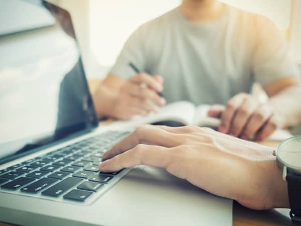 Close up of person typing with colleague taking notes