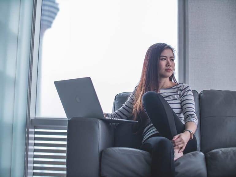 Woman sitting on coach with computer thinking about taking the PMP exam